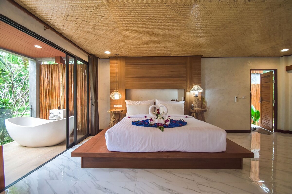 Un dormitorio moderno con una cama grande, una bañera integrada y vistas al verdor.