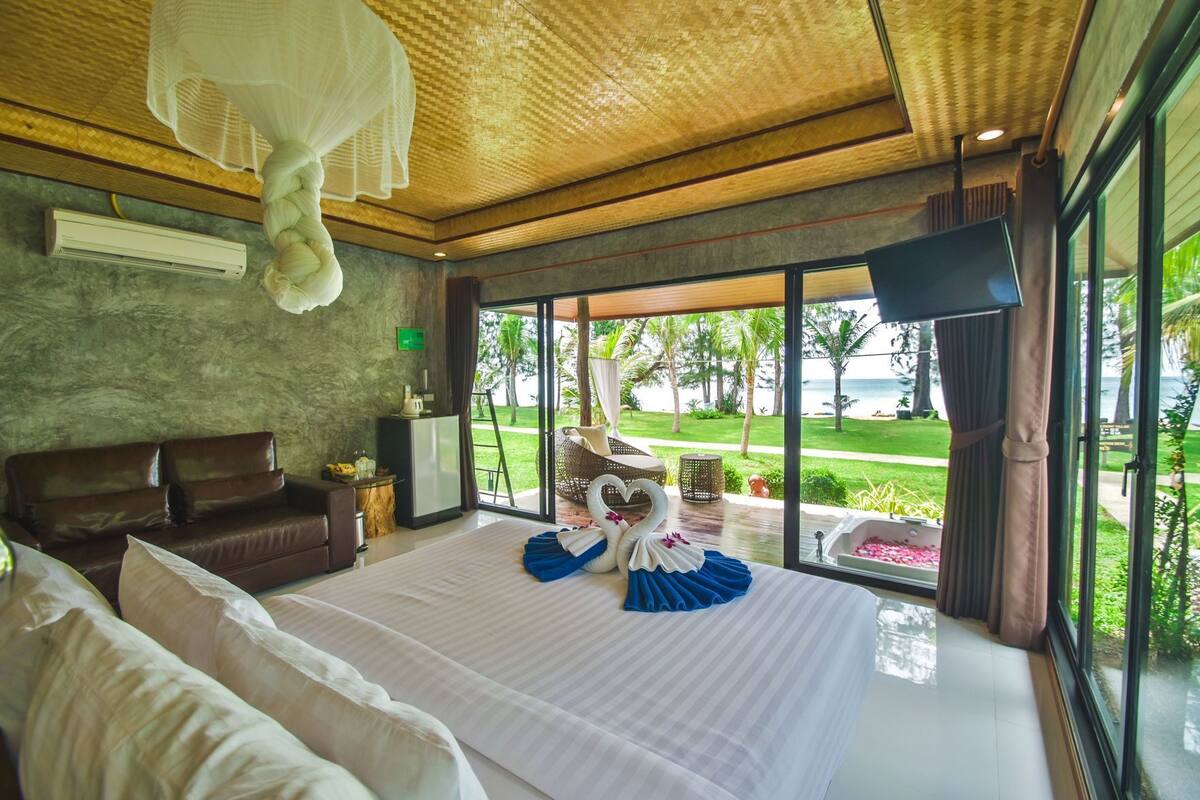 A bedroom with a large bed, a sofa, a TV, and a view of the outdoors.
