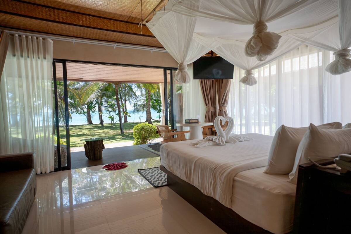 A bedroom with a large bed, a TV, and a view of the beach.