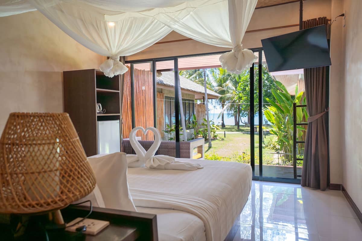 A hotel room with a bed, a bedside lamp, a TV, and a view of the outdoors.