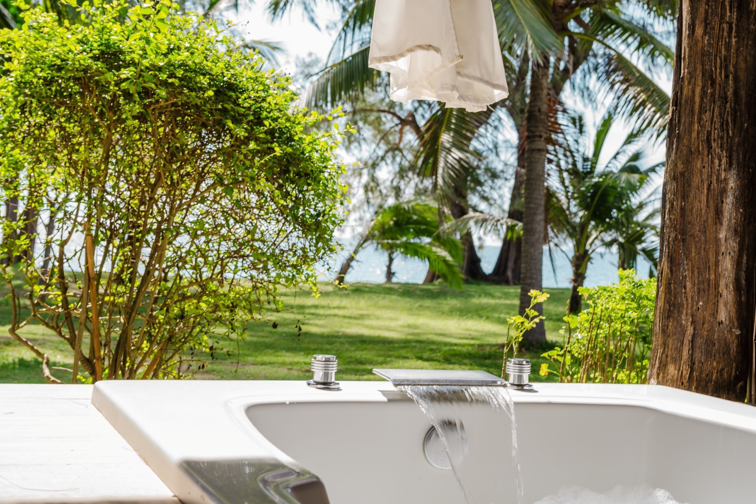 Eine Badewanne mit Wasserhahn, umgeben von üppiger Vegetation und Palmen.