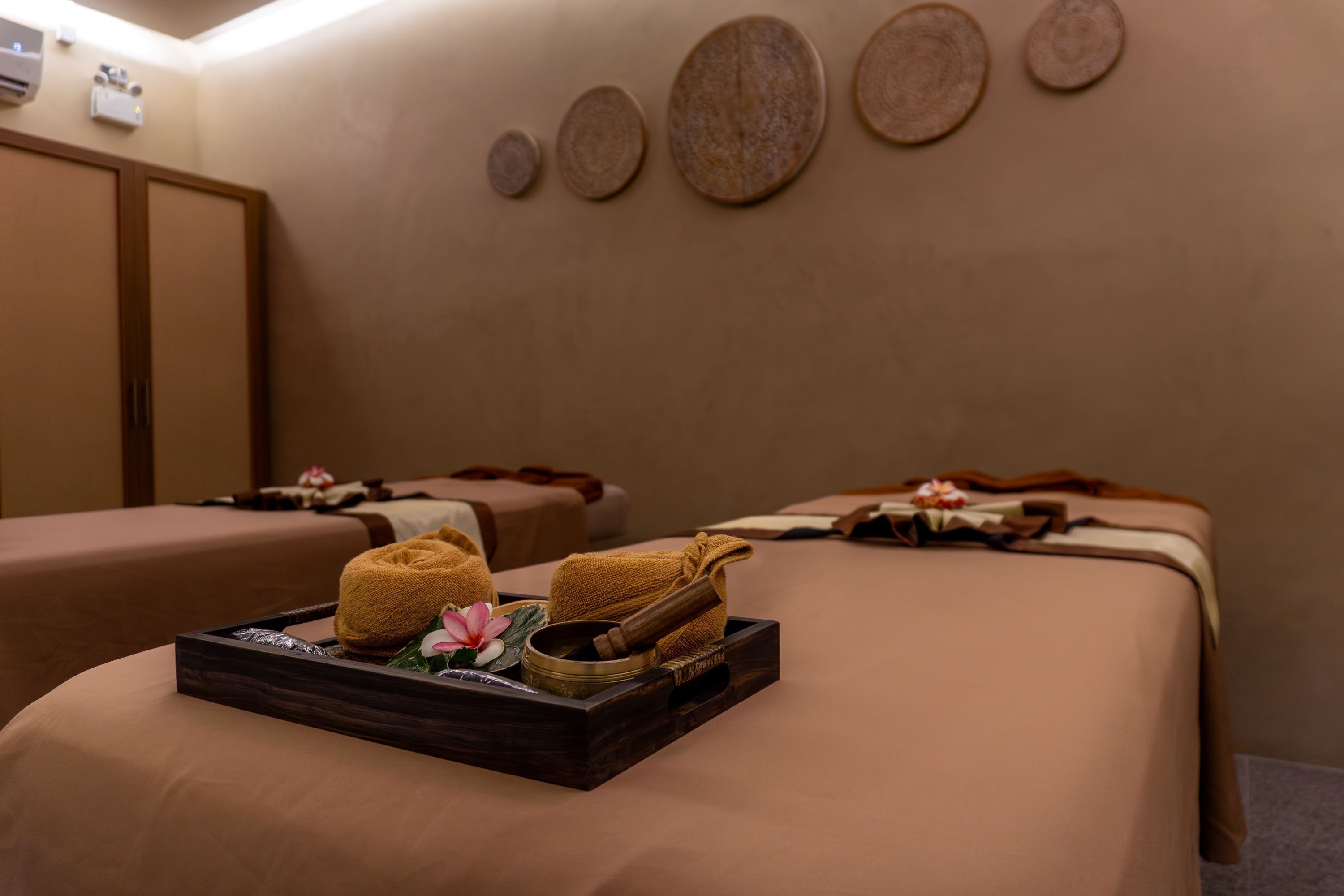 A spa room with two massage tables, each with towels and a wooden tray containing a massage tool and a flower.