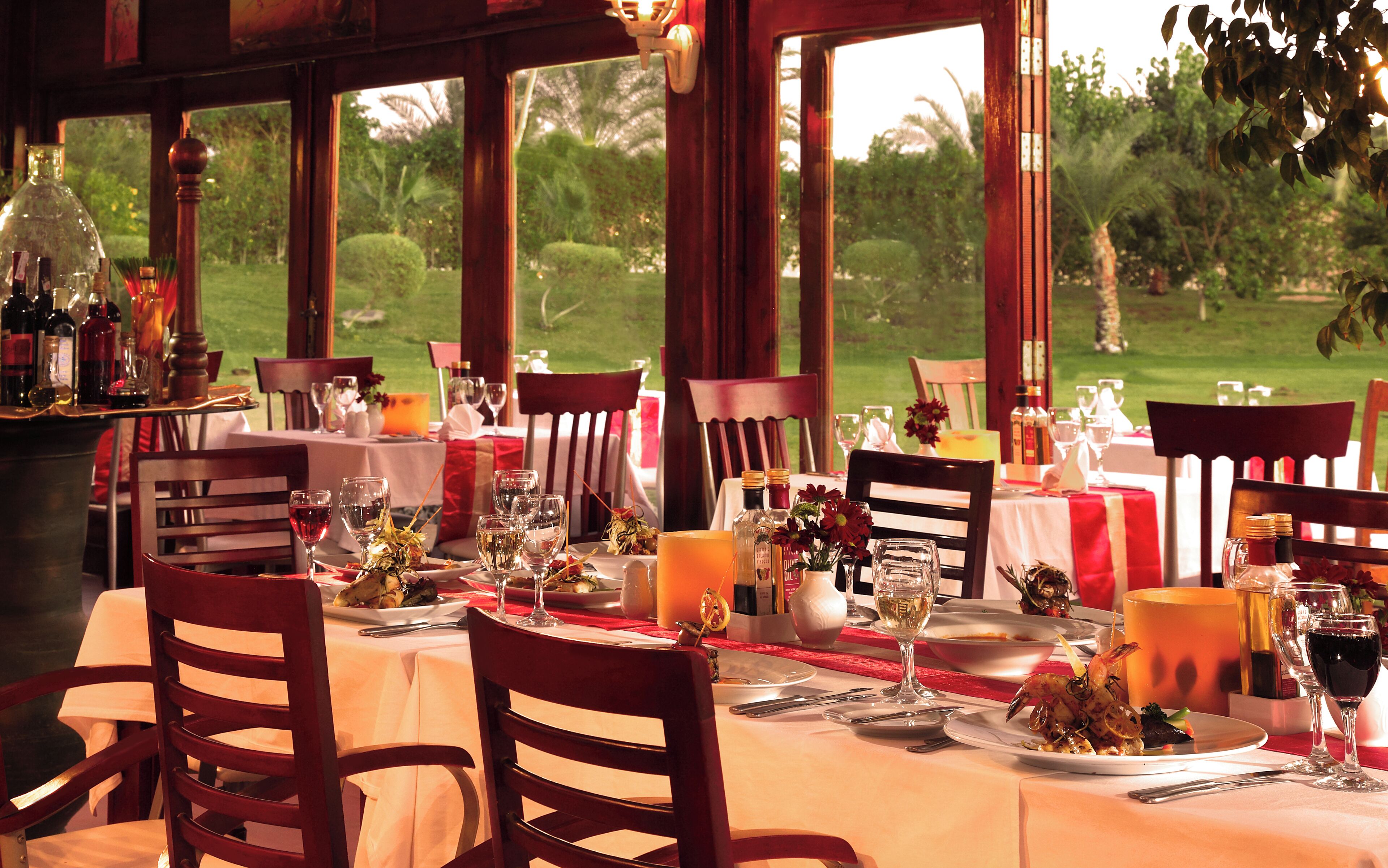Una mesa de comedor lista para una comida, con sillas, copas de vino y vistas al exterior.