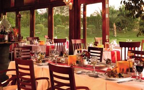 Una mesa de comedor lista para una comida, con sillas, copas de vino y vistas al exterior.