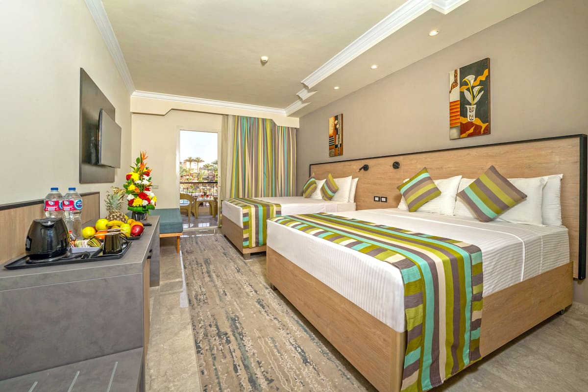A hotel room with two beds, a desk with a coffee maker, fruit, and flowers.