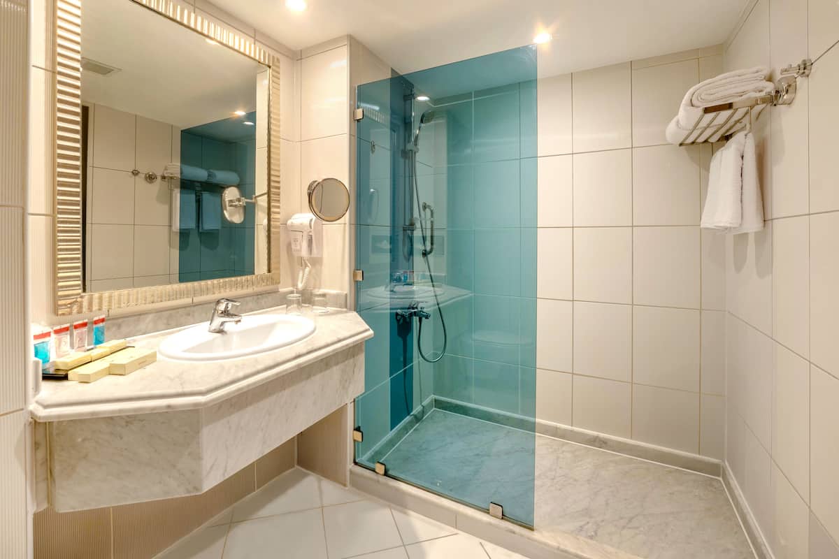 A modern bathroom with a large mirror, two sinks, a glass-enclosed shower, and a towel rack.