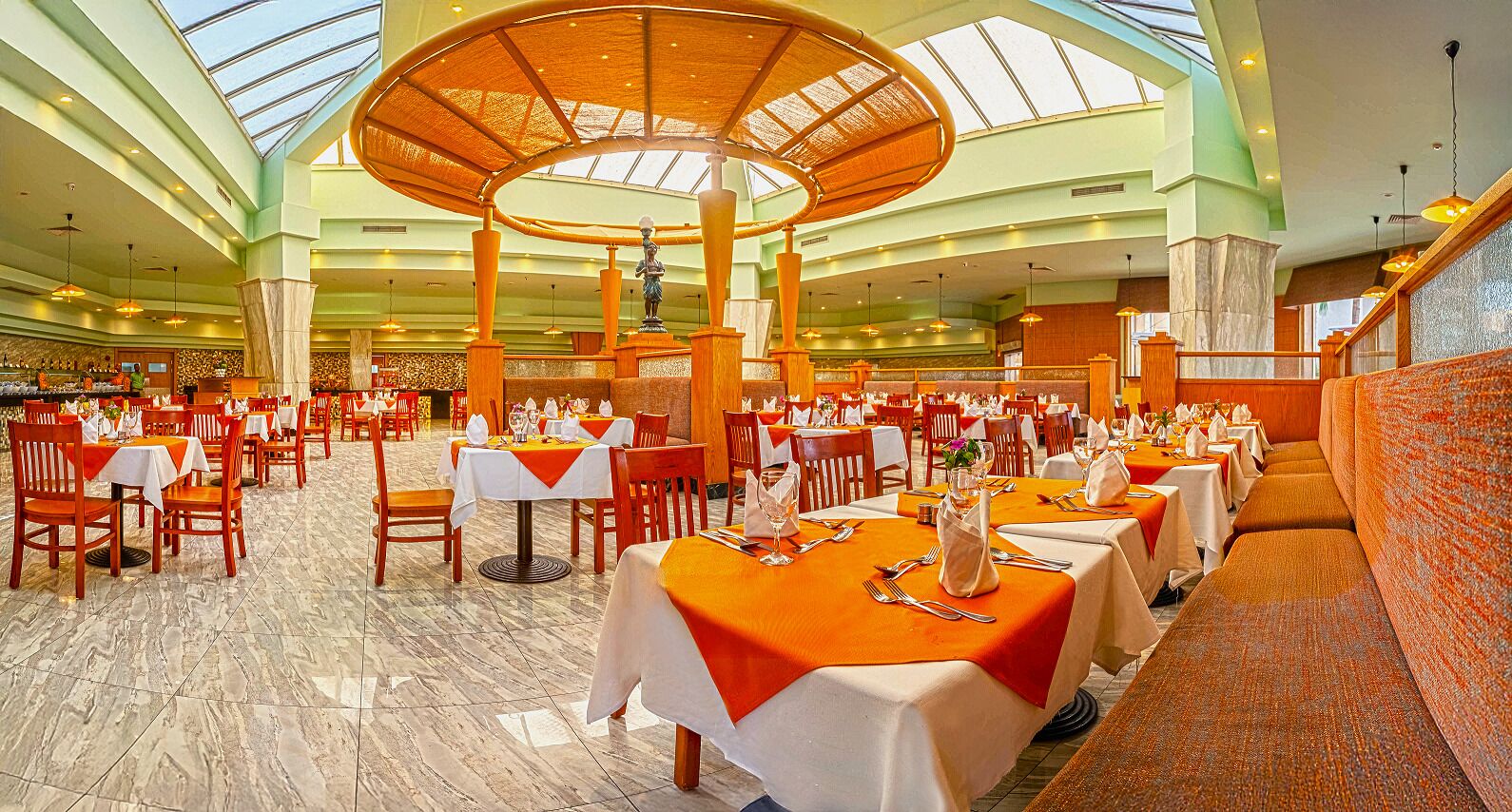 A spacious dining area with multiple tables and chairs, a central decorative column, and a high ceiling with skylights.