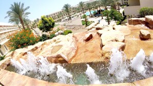 A water feature with a cascading waterfall, surrounded by rocks and palm trees. - Xperience Kiroseiz Premier (Sharm El Sheikh)
