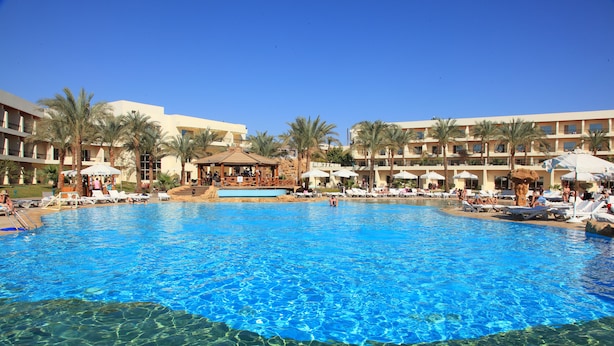 A large swimming pool with clear blue water, surrounded by palm trees and hotel buildings. - Xperience Kiroseiz Premier (Sharm El Sheikh)