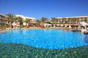 A large swimming pool with clear blue water, surrounded by palm trees and hotel buildings. - Xperience Kiroseiz Premier (Sharm El Sheikh)