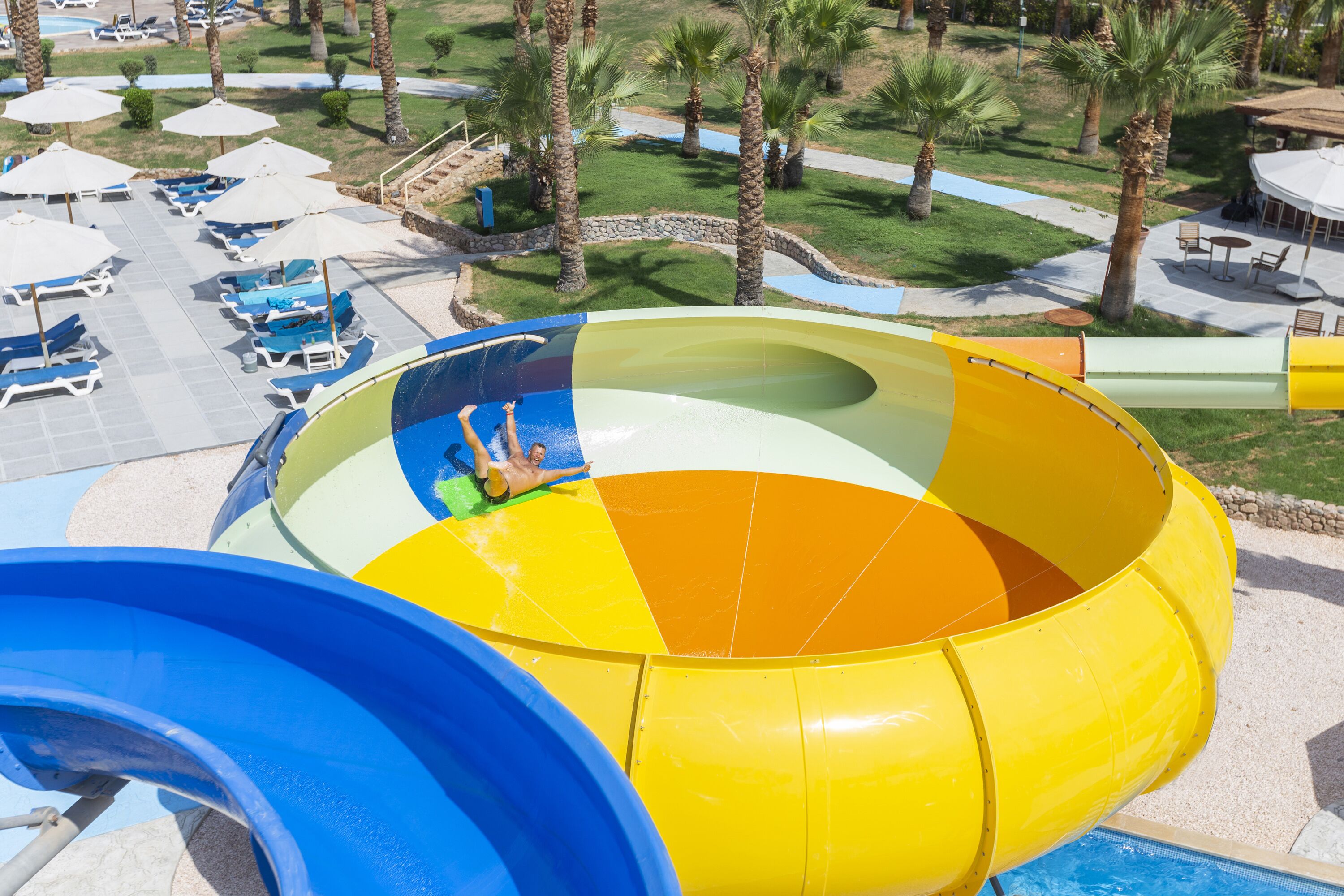 Un toboggan aquatique avec une personne en haut, entouré de chaises longues et de parasols.