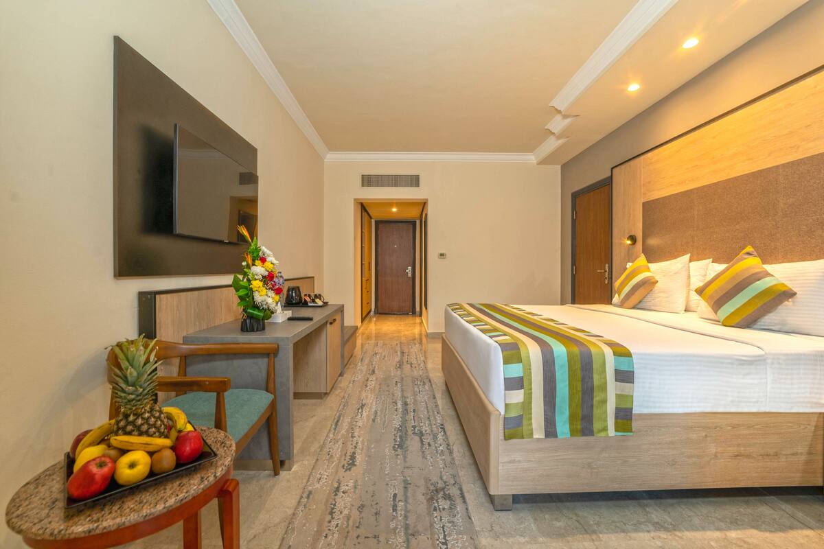 A hotel room with a bed, a desk, a chair, and a fruit bowl.