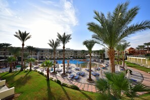 Un resort con zona de piscina, palmeras y sillones de descanso.
