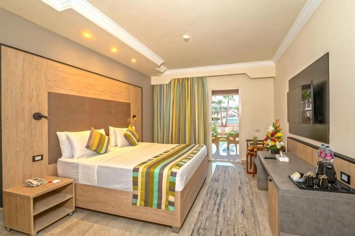 A hotel room with a bed, bedside table, TV, and a view of the outdoors.