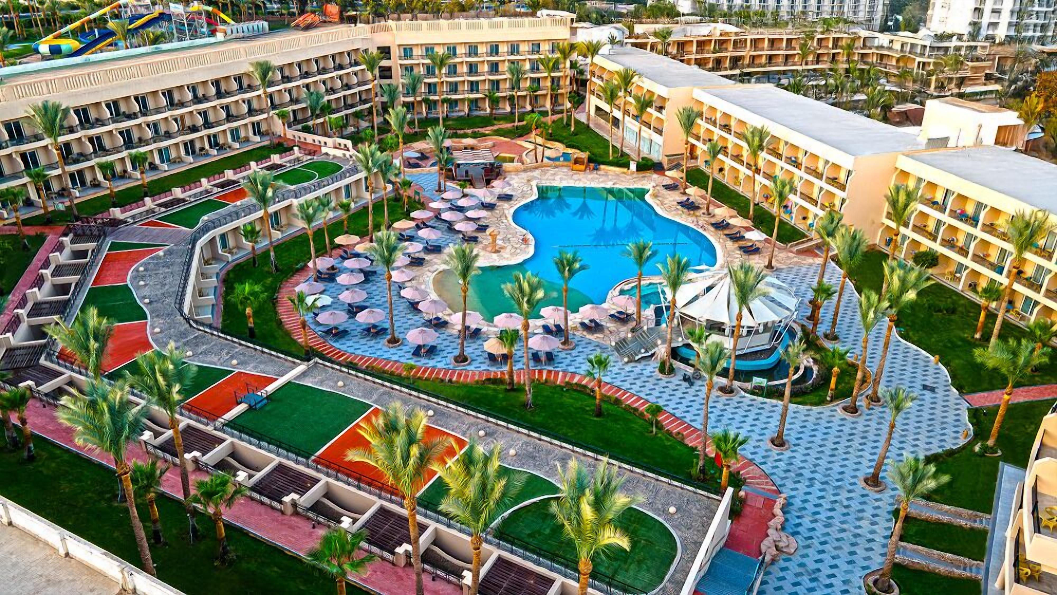 Een resort met een centraal zwembad, meerdere balkons en palmbomen.
