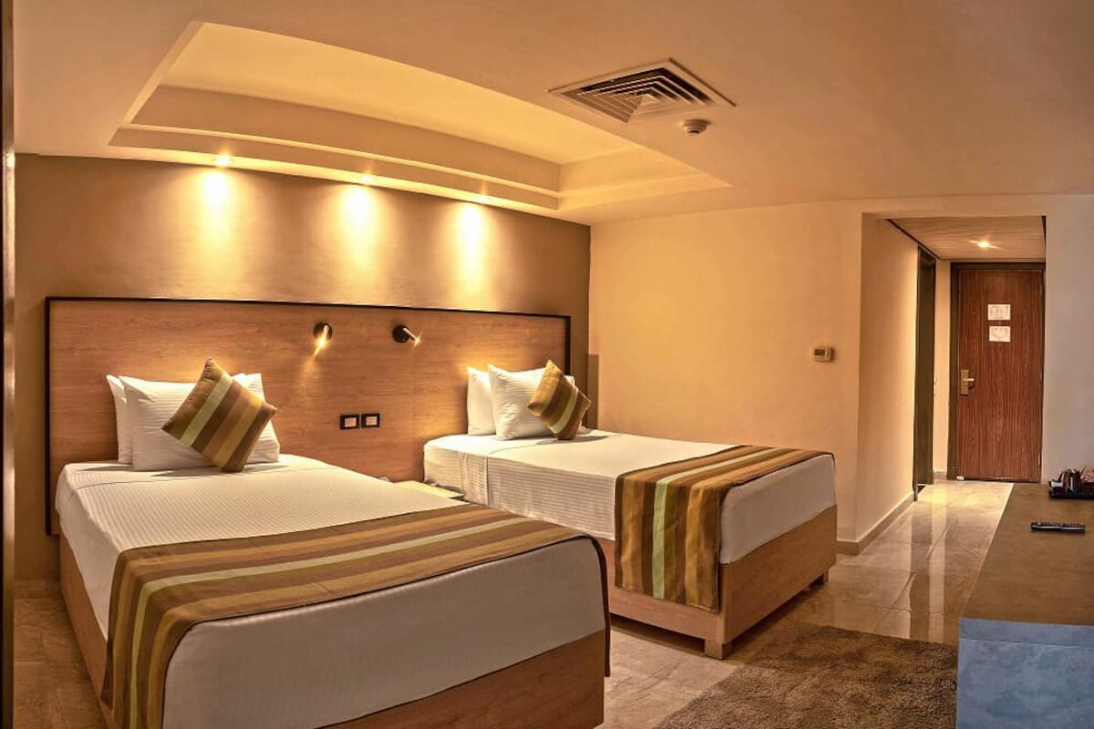 A hotel room with two beds, a sitting area with a table and chairs, and a view of the outdoors.