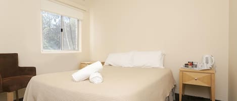 Una habitación de hotel con cama, una silla, una mesita de noche con cafetera y ventana con persianas.