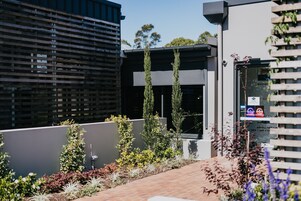 A modern building with a glass facade, a paved outdoor area with plants, and a sign indicating a dining room.