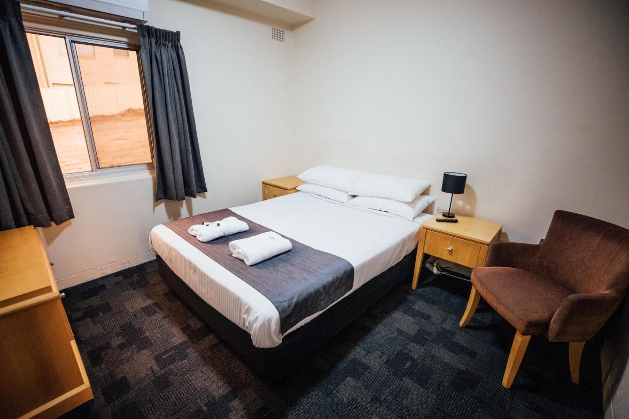 Ein Hotelzimmer mit Bett, Nachttisch, Stuhl, Schreibtisch und einem Fenster mit Vorhängen.
