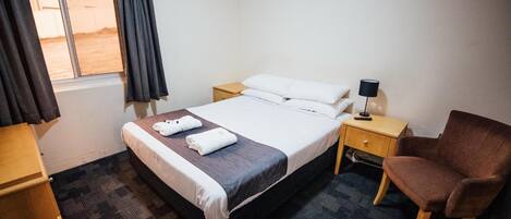 Habitación de hotel con cama, mesita de noche, silla, escritorio y ventana con cortinas.