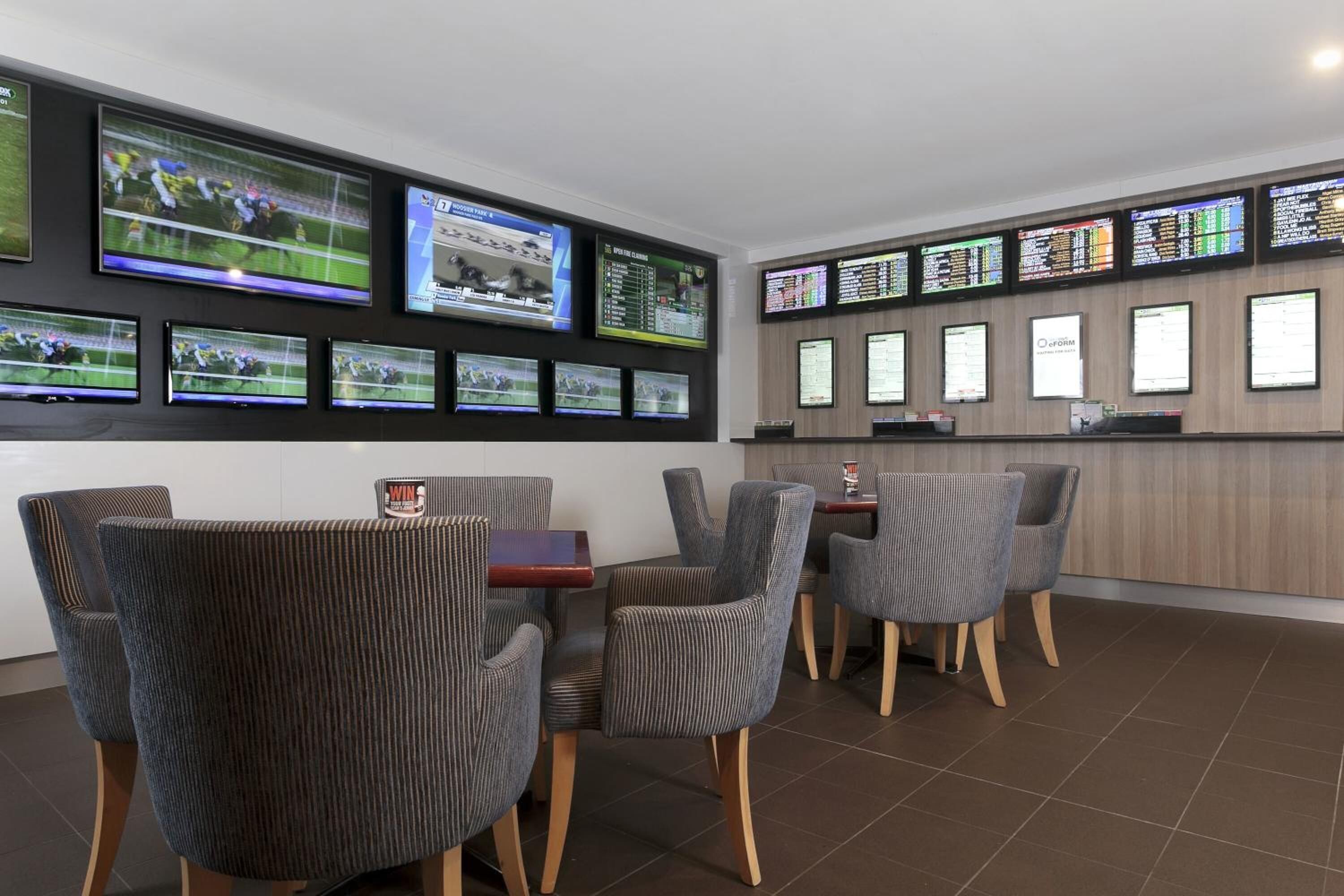 A modern hotel lobby with multiple screens displaying sports events, comfortable seating, and a wooden reception desk.