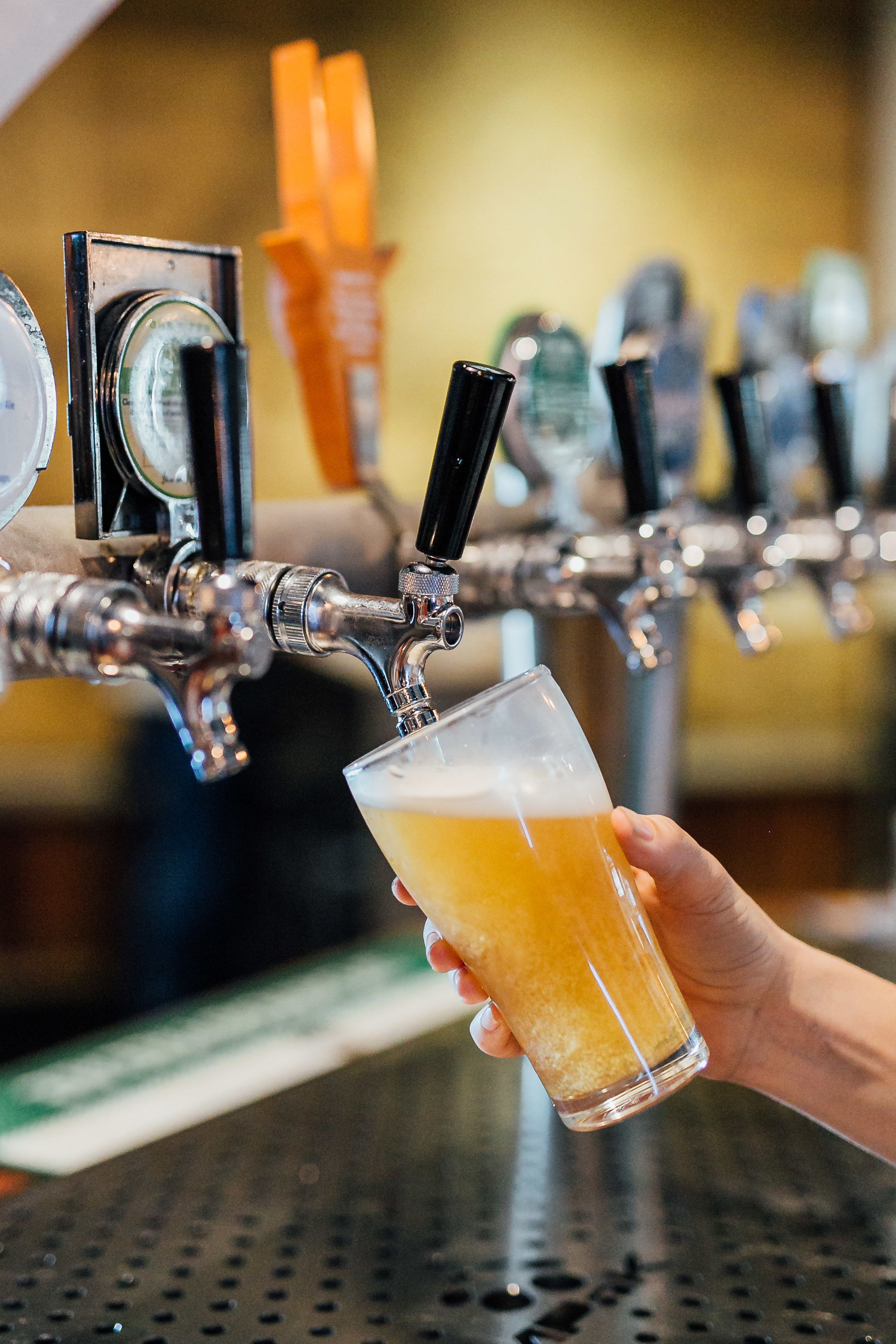 A hand holding a glass of beer at a tap.