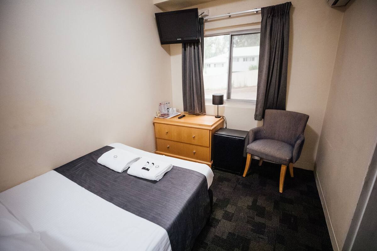A hotel room with a bed, a desk with a chair, a dresser, a TV, and a window with curtains.