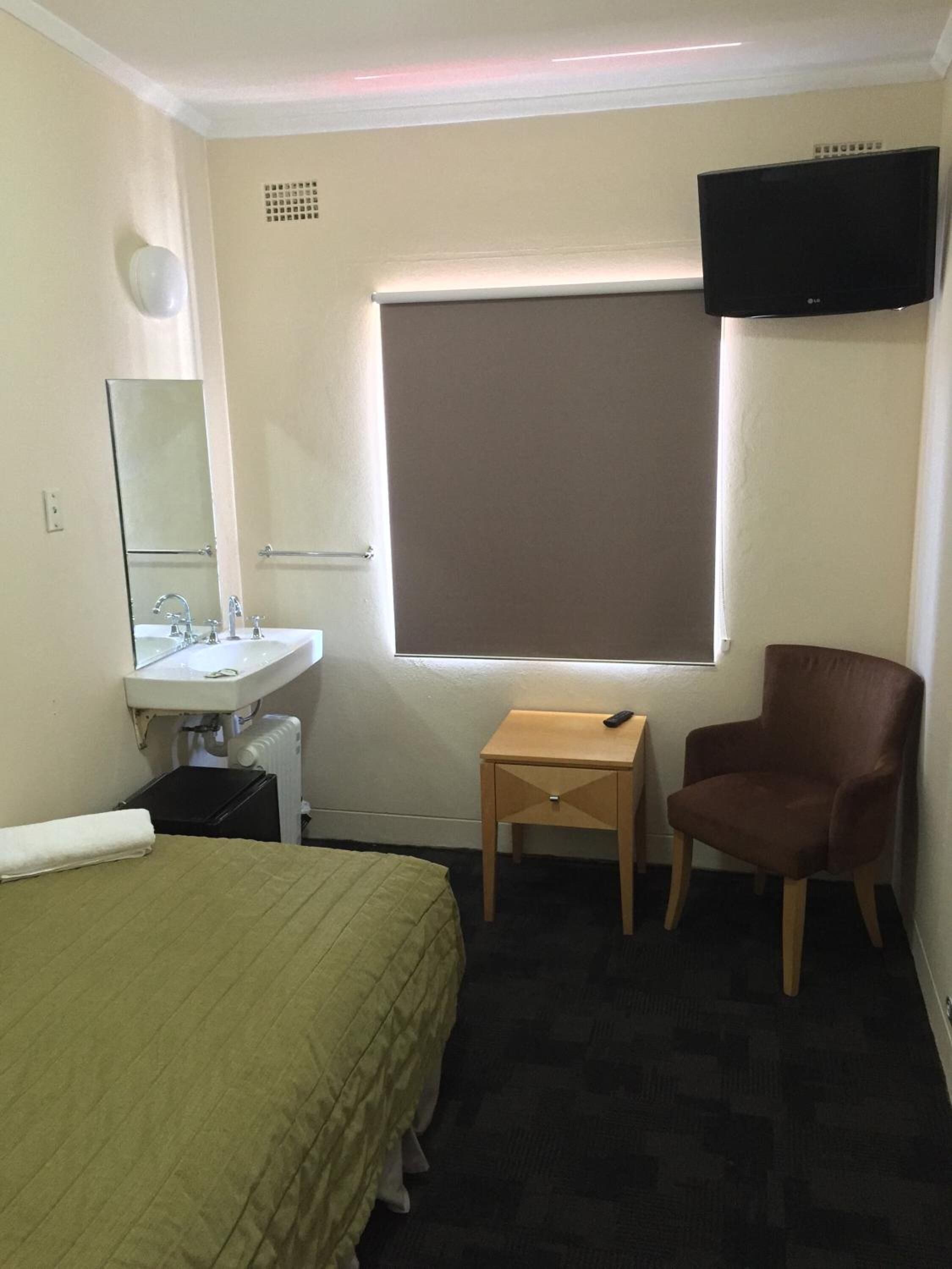 A hotel room with a bed, a bedside table, a chair, a TV, a window, and a bathroom with a sink and mirror.