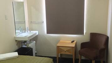 A hotel room with a bed, a bedside table, a chair, a TV, a window, and a bathroom with a sink and mirror.