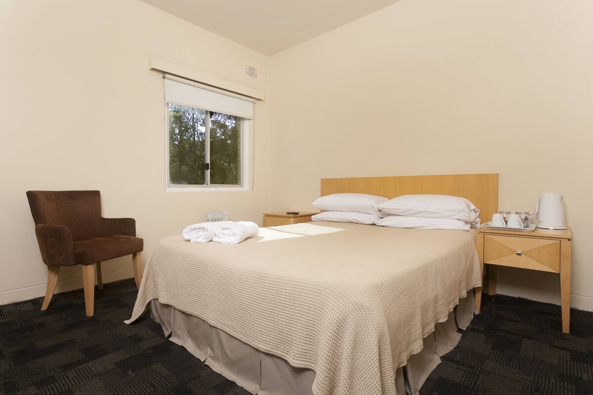 A hotel room with a bed, a chair, a nightstand, a window, and a view of trees.
