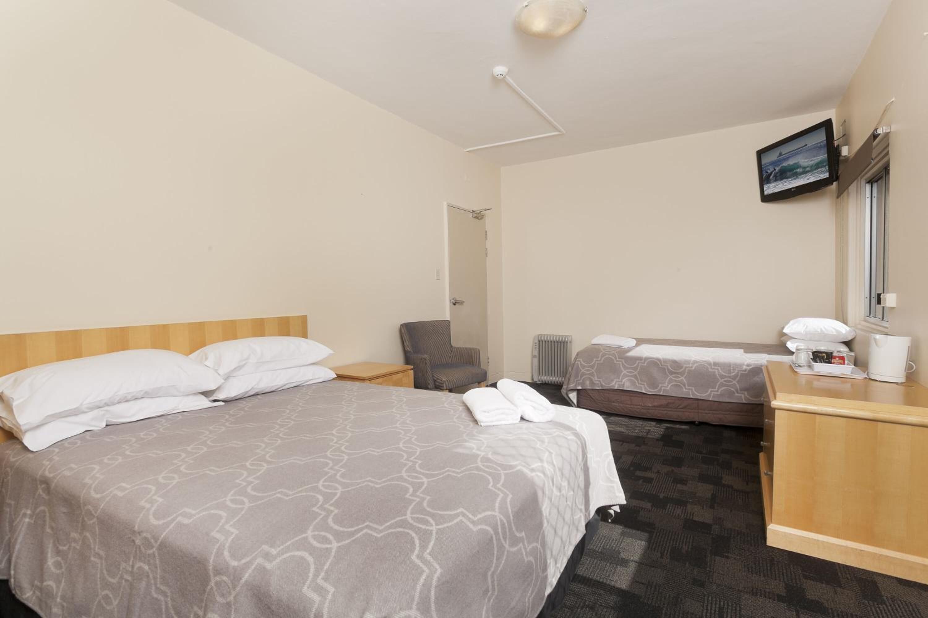 A hotel room with two beds, a desk, a chair, a television, and a window.