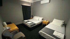 Habitación de hotel con dos camas, un escritorio, una silla y una mesita de noche con lámpara.
