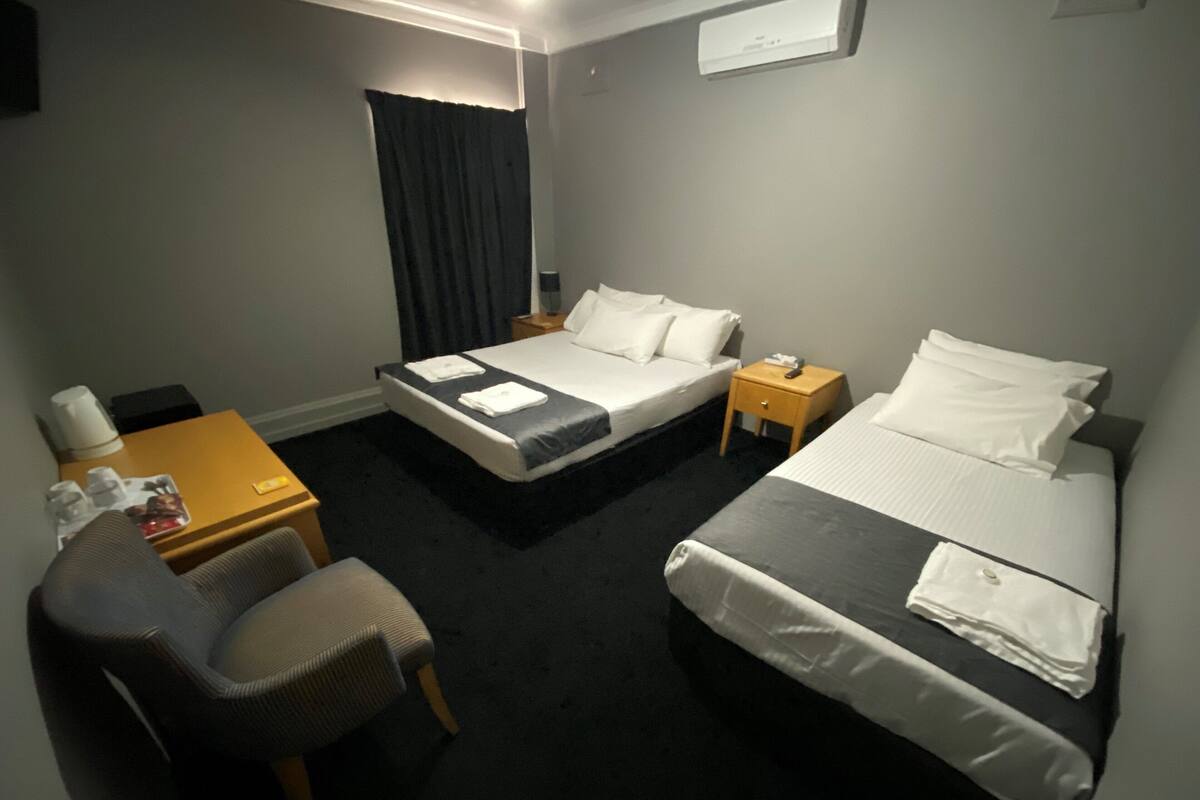 A hotel room with two beds, a desk, a chair, and a small table with a lamp.