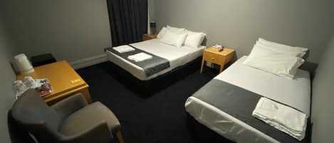 Ein Hotelzimmer mit zwei Betten, einem Schreibtisch, einem Stuhl und einem kleinen Tisch mit einer Lampe.