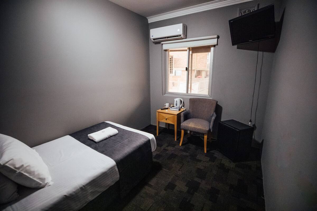 A small hotel room with a single bed, a chair, a desk, and a TV.
