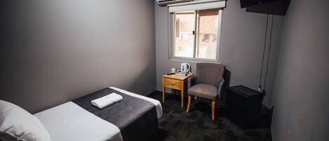 A small hotel room with a single bed, a chair, a desk, and a TV.