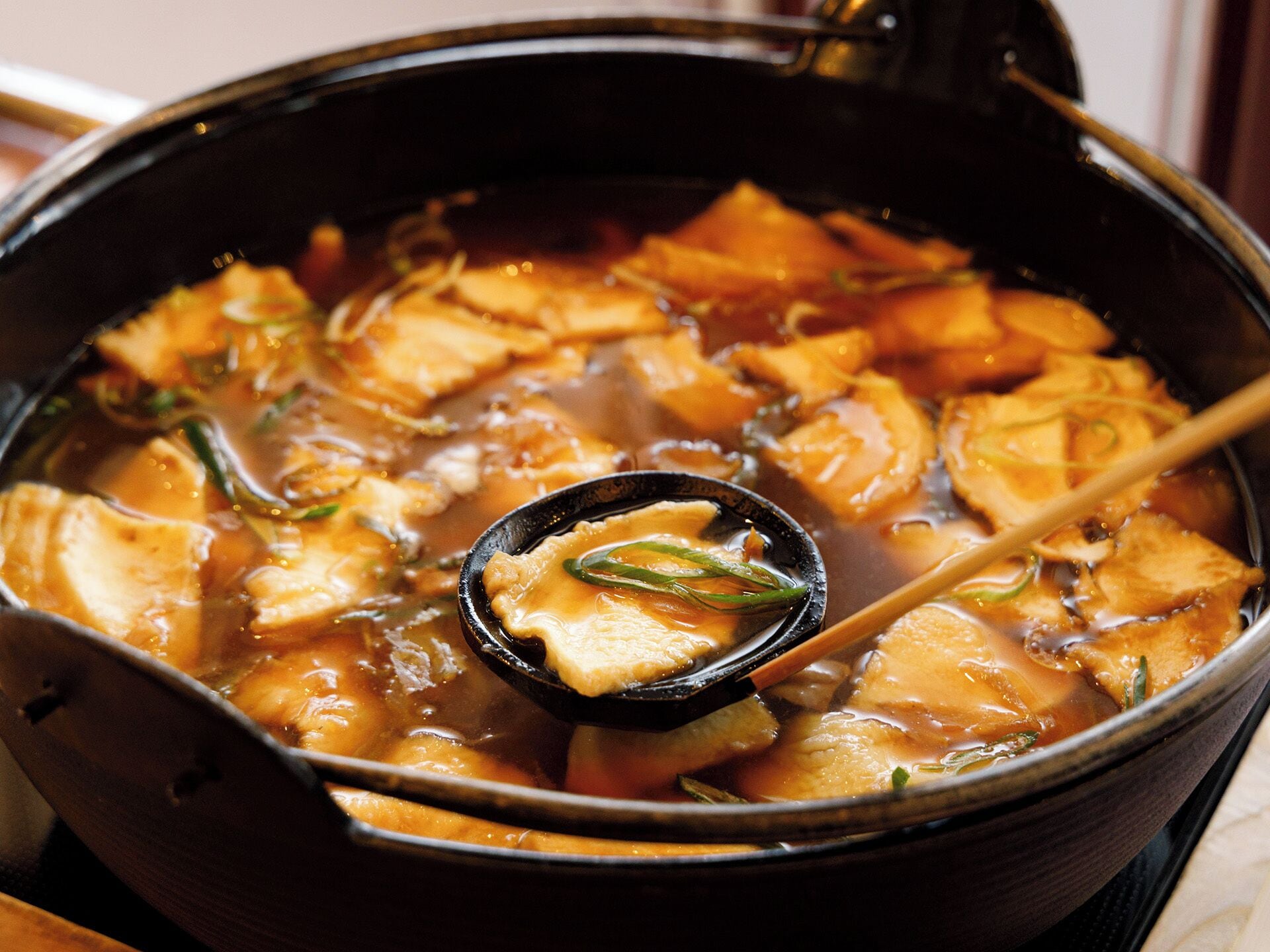 A close-up of a hot pot dish with tofu and vegetables in a black pot.