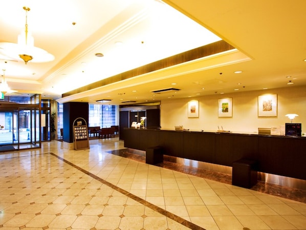 A hotel lobby with a reception desk, seating area, and a large window.