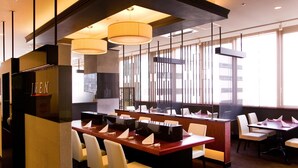Ein modernes Restaurant mit einer zentralen Bar, verschiedenen Sitzgelegenheiten und großen Fenstern für natürliches Licht.