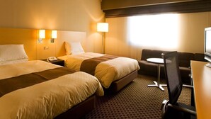 Ein Hotelzimmer mit zwei Betten, einem Schreibtisch, einem Sessel und einem Fernseher.