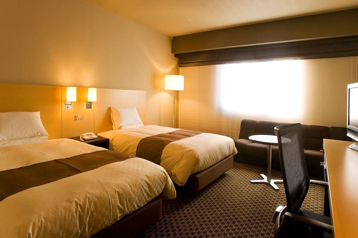 A hotel room with two beds, a desk, a chair, and a TV.