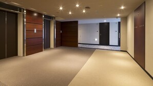 Ein moderner Hotelgang mit Teppichboden, Holzwandverkleidung und einem sichtbaren Aufzug.