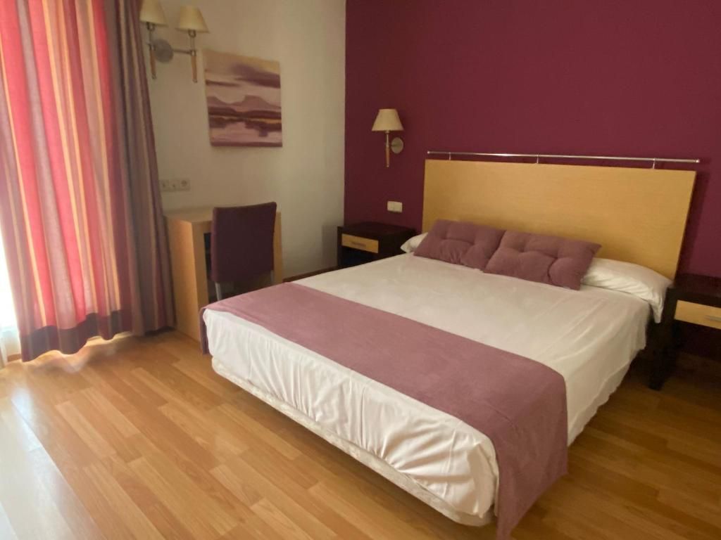 A hotel room with a large bed, wooden flooring, a desk, and a nightstand.