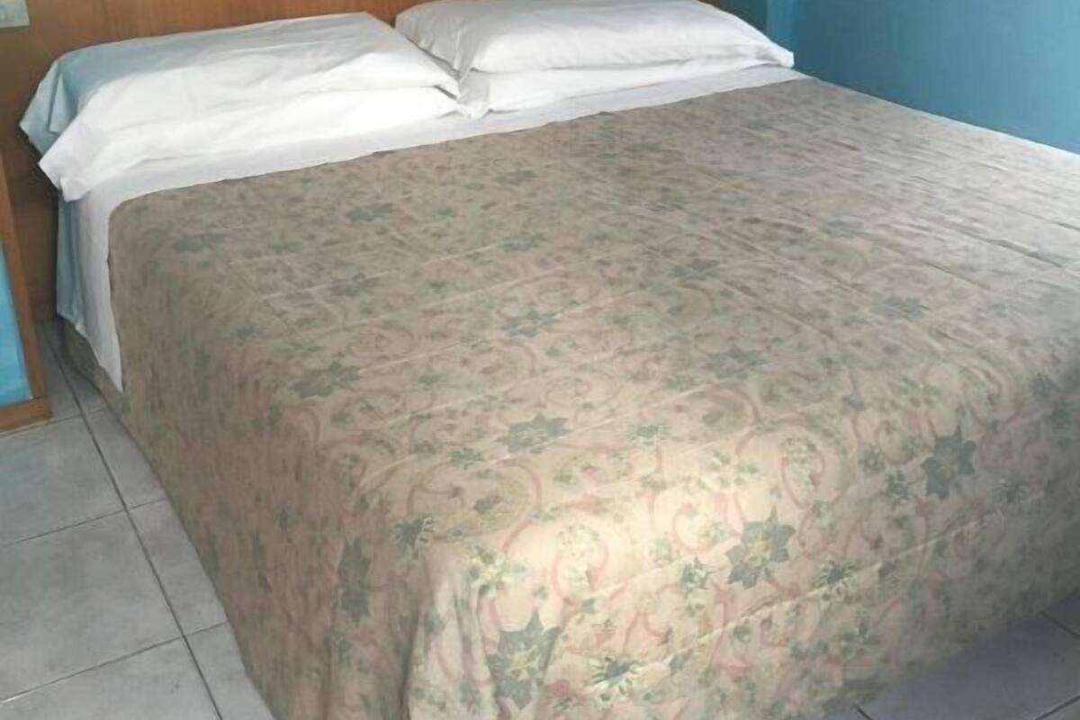 A single bed with a floral bedspread and white pillows in a room with blue walls and a wooden headboard.