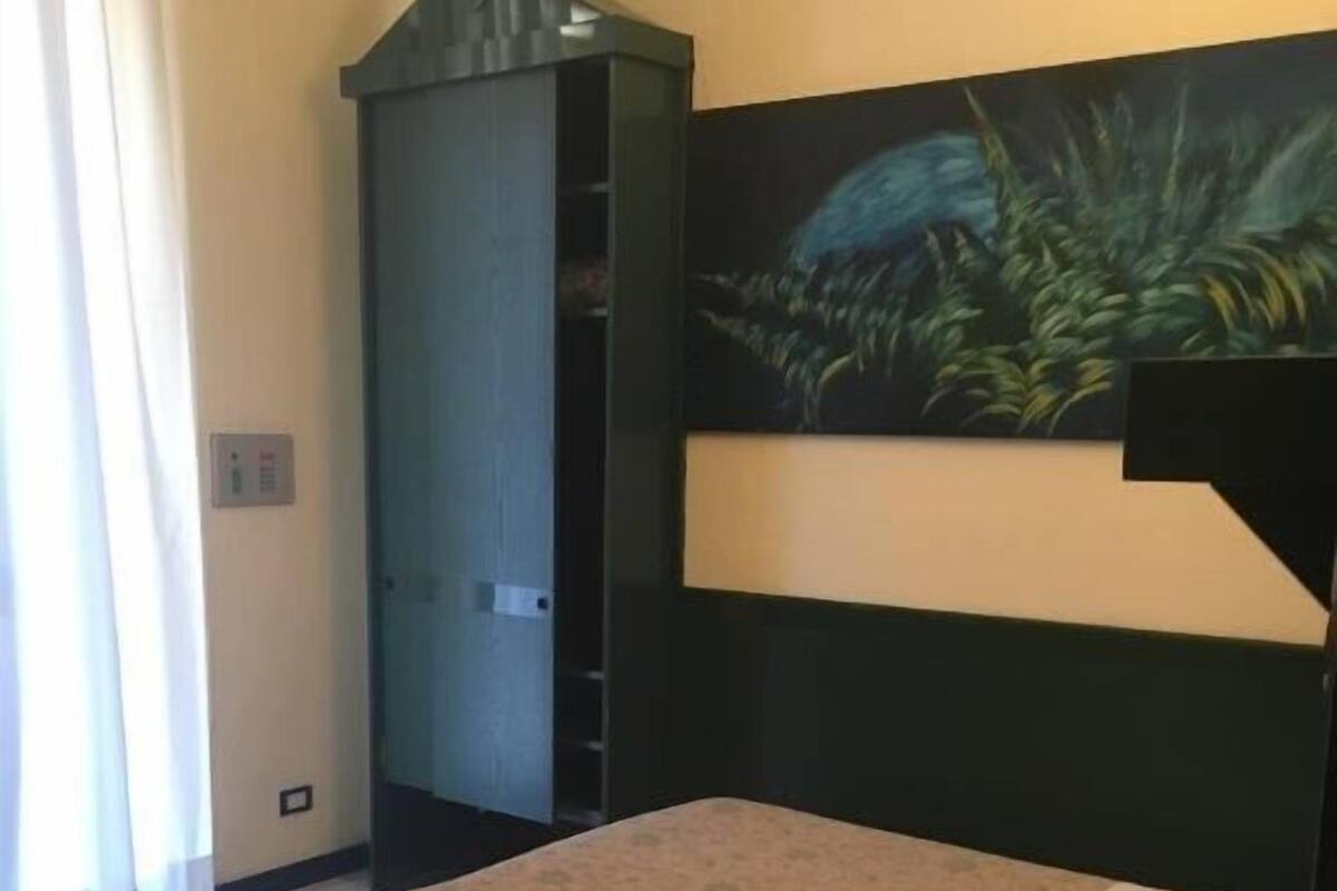 A hotel room with a bed, a wardrobe, and a painting on the wall.