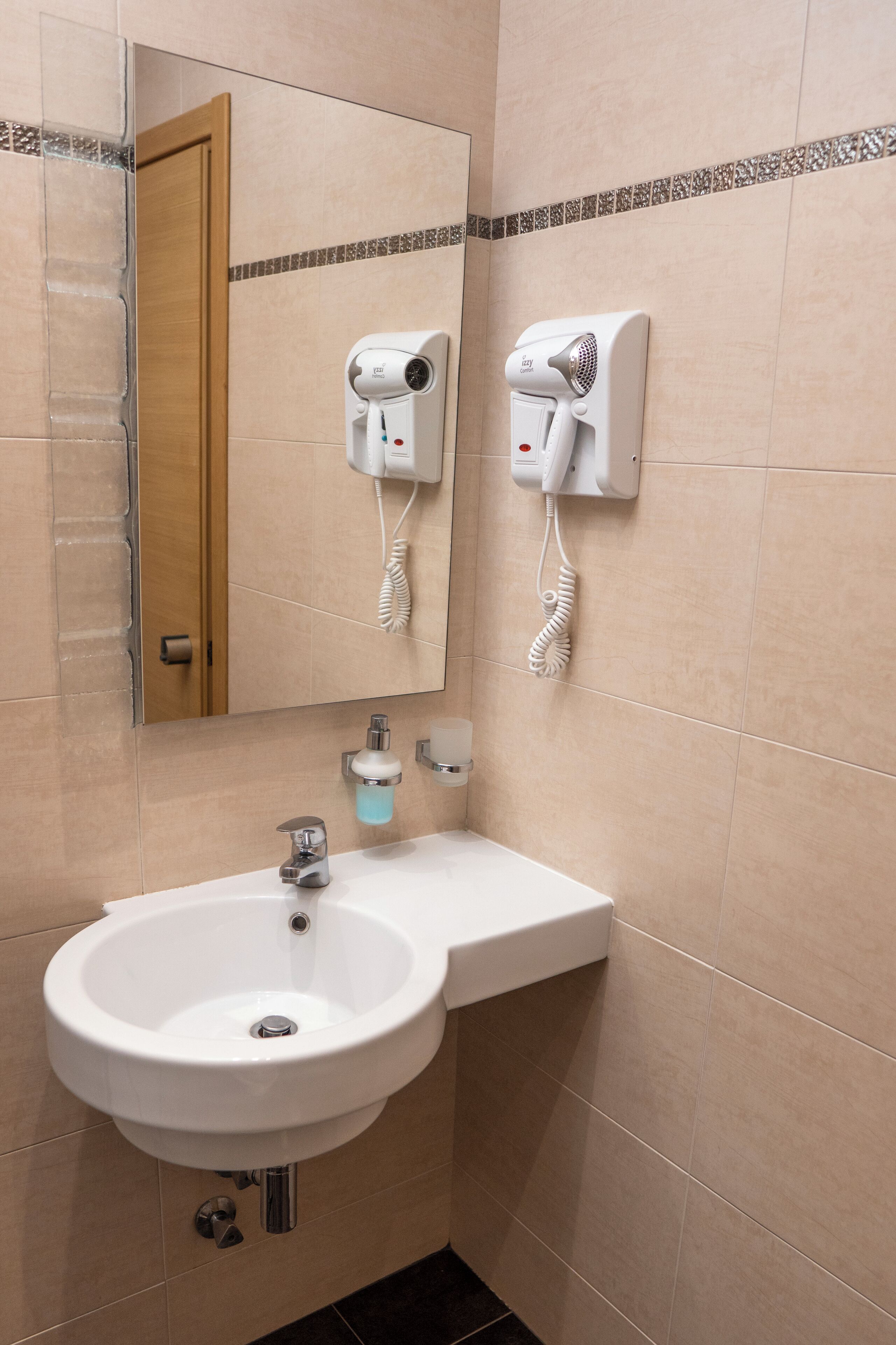 A bathroom with a sink, mirror, and two hair dryers mounted on the wall.