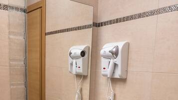 A bathroom with a sink, mirror, and two hair dryers mounted on the wall.