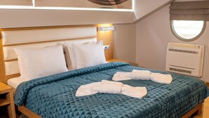 A modern hotel room with a wooden bed, a blue quilted bedspread, and neatly folded towels on the bed. - Hotel Epavlis Eleftheriadi (Katerini)