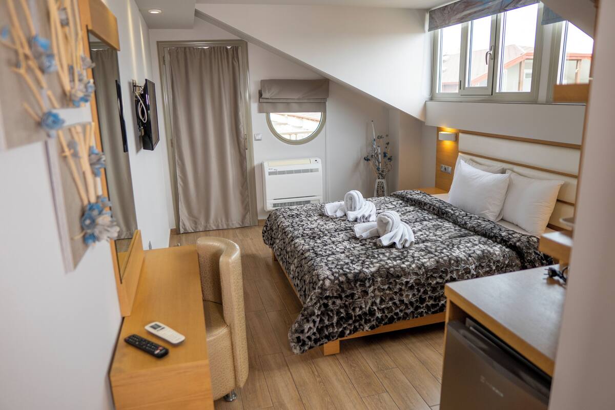 Ein Hotelzimmer mit einem Bett, einem Schreibtisch, einem Stuhl, einer Fernbedienung und einem Fenster mit Vorhängen.