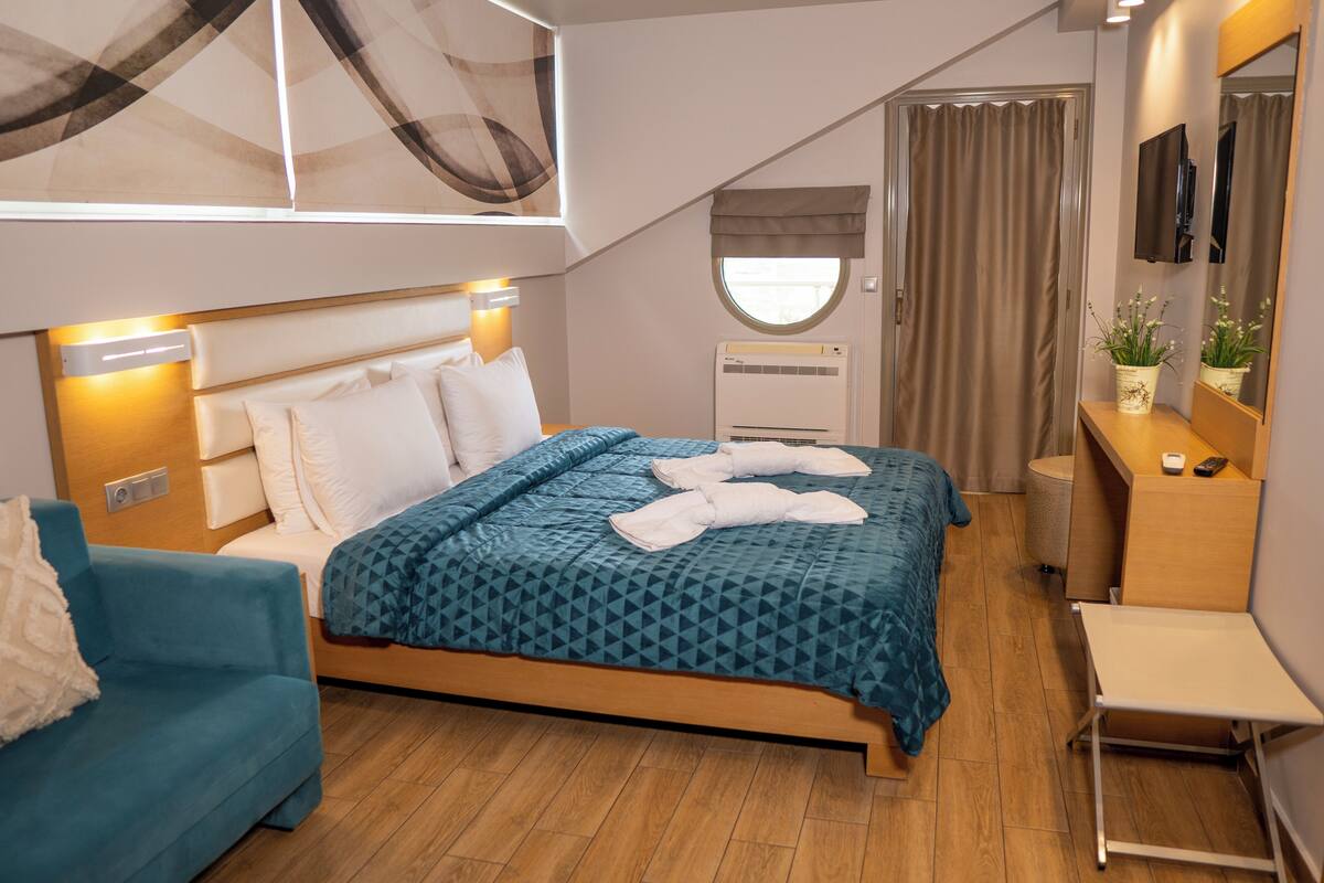 Ein modernes Hotelzimmer mit einem Bett, einem Schreibtisch, einem Stuhl, einem kleinen Tisch, einem Fernseher und einem Fenster mit Vorhängen.